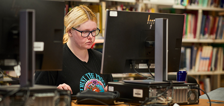 student with glasses on working on a computer in the library