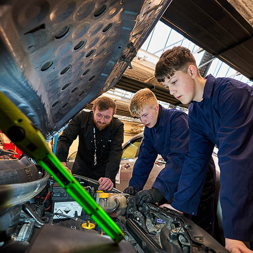 two students leaning over a car bonnet with their lecturer