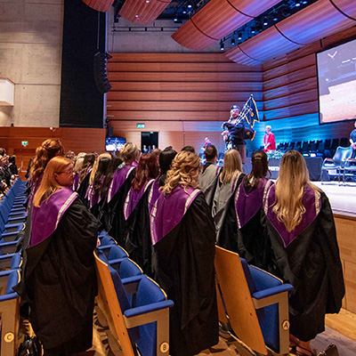 Students standing while the piper plays during Graduation