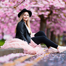 veronika sitting on a pavement in a pink skirt with a pink blossom tree behind her