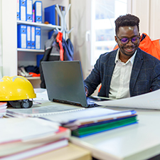 person working at a desk in an office with a hard hat and high vis jacket