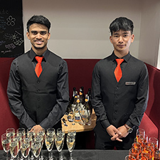 tashi and nabin standing next to a table serving drinks