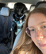 Picture of a student sitting in a car with a dog in the background